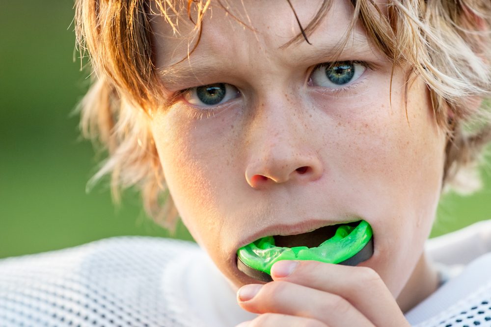 young boy foot ball player with athletic mouth guard he is pulling out of his mouth